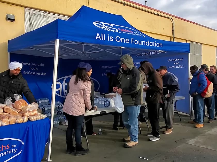 Volunteers serving food and water to a line of people at the All is One Foundation tent