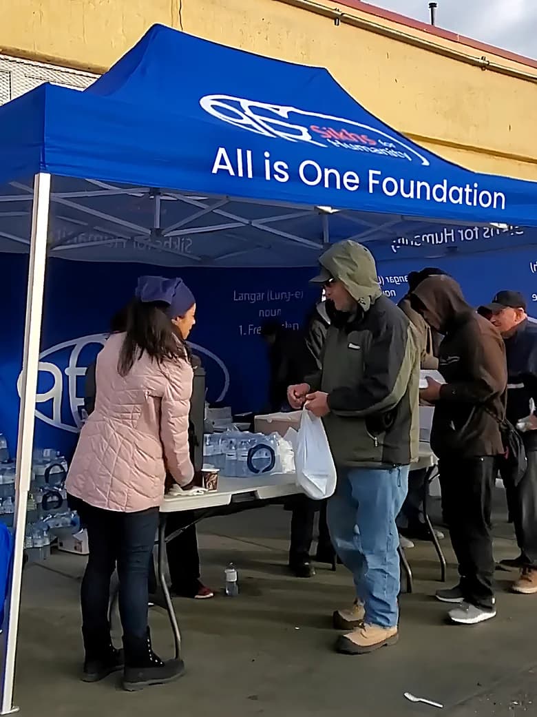 People lining up at the All is One Foundation tent for food and water