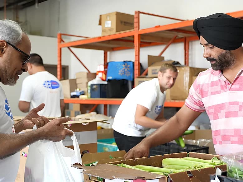 Volunteers in All is One shirts packing fresh produce into bags at the food bank