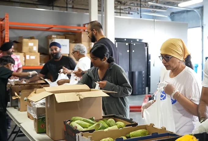 Volunteers of all ages packing grocery hampers from boxes of vegetables