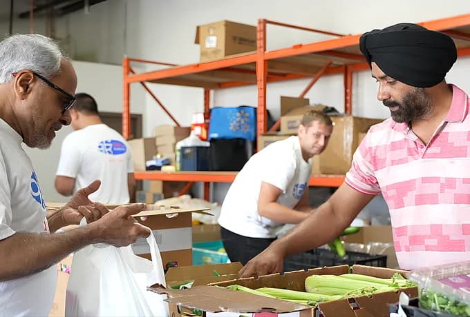 Volunteers in All is One shirts sorting fresh produce into bags
